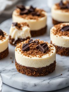 several desserts are arranged on a marble platter with chocolate crumbs and white frosting