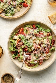 two plates filled with salad next to glasses of wine and bread on a table top