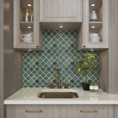 a kitchen with gray cabinets and white counter tops, gold faucets and a green tile backsplash