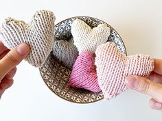 two hands holding knitted hearts in a bowl