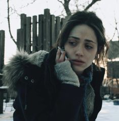 a woman is talking on her cell phone outside in the snow while wearing a winter coat