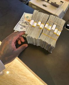 a person holding money in front of a stack of cash