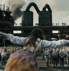 a woman with her arms outstretched in front of a large group of people and smokestacks