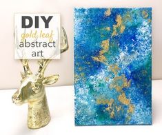 a gold deer head is next to an abstract art piece on a white table with a sign that says diy