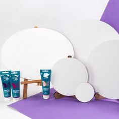 three white plates and two cream tubes on a purple background with a wooden easel