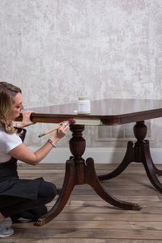 a woman kneeling down to paint a table