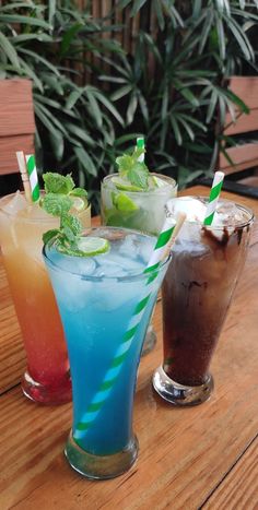 three different colored drinks sitting on top of a wooden table next to eachother