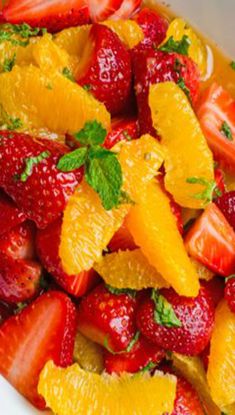 fresh fruit salad with oranges, strawberries and mint in a white serving dish