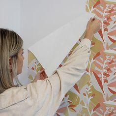 a woman is painting a floral wallpaper with white paint on it and she has her hands in the air