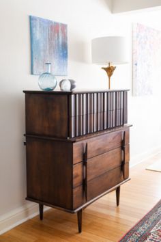 a wooden dresser sitting on top of a hard wood floor next to a lamp and painting