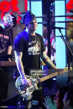 a man with blue hair and piercings playing an electric guitar in front of a microphone