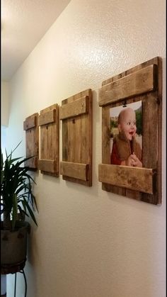 three wooden frames hanging on the wall with a baby's face in them and a potted plant