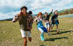 a group of young people running across a grass covered field next to a lake in the background