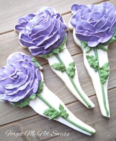 three cookies decorated with purple flowers on top of a wooden table next to each other