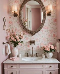 a bathroom with pink walls and flowers on the counter top, along with a large round mirror