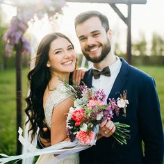 a man and woman standing next to each other in front of a gazebo holding flowers