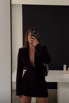 a woman taking a selfie in front of a mirror wearing a black dress and heels