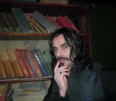 a man with long hair is talking on his cell phone in front of bookshelves