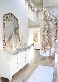 a white christmas tree in the middle of a living room next to a stair case