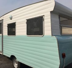 an old blue and white camper parked in a parking lot next to another trailer