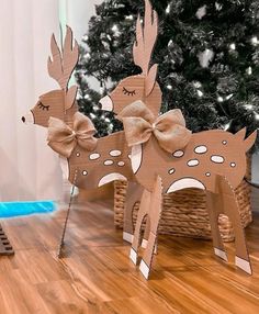 two wooden deer standing on top of a hard wood floor next to a christmas tree