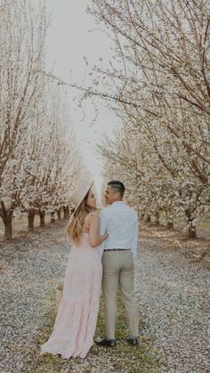 a man and woman standing next to each other in front of trees with blossoming branches