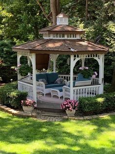 a white gazebo sitting in the middle of a lush green park with pink flowers