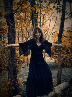 a woman standing in the woods with her arms spread out and wearing a black dress