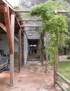 a truck parked under a wooden structure next to a tree and grass covered yard area