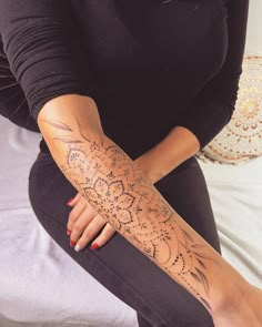 a woman sitting on top of a bed with her arm covered in intricate designs and tattoos