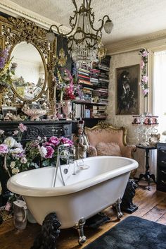 a bathtub with flowers on the floor in front of a mirror and chandelier