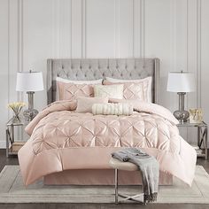 a bed with pink comforter and pillows in a room next to two nightstands