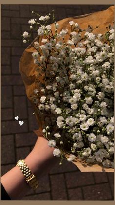 a bouquet of white flowers is held by someone's hand on a brick sidewalk