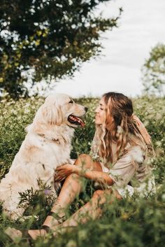 a woman is sitting in the grass with her dog and smiling at each other while they both have their heads close to one another