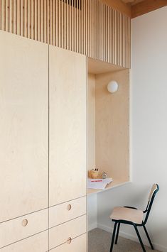 a chair sitting in front of a wooden cabinet next to a white wall with wood slats on it