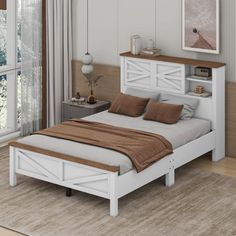 a white bed with brown pillows in a bedroom next to a large window and wooden flooring