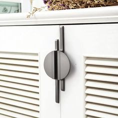 a white cabinet with shutters and a round knob on the front door, next to a basket full of dried flowers