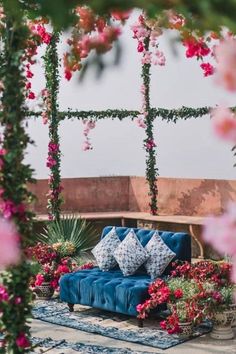 a blue couch sitting on top of a lush green field covered in pink and red flowers