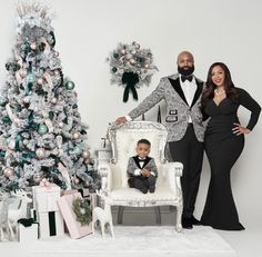 a man and woman standing next to a small child in front of a christmas tree