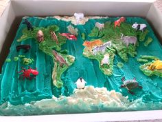 a cake in the shape of a world map with animals and plants on green icing