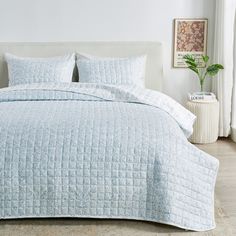 a bed with blue quilted bedspread and pillows in a white room next to a potted plant