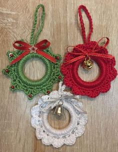 three christmas ornaments hanging on a wooden surface with bells and ribbons attached to each ornament