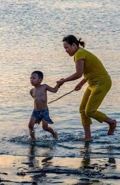 a woman holding the hand of a child who is walking in water with a rope