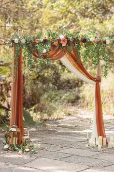 an orange and white wedding arch decorated with flowers, greenery and candles for the ceremony