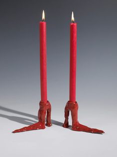 two red candles sitting next to each other on top of a white surface with one candle in the shape of an animal's foot