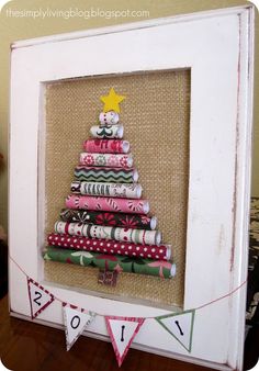 a christmas tree made out of rolled up wrapping paper in a white frame on a table