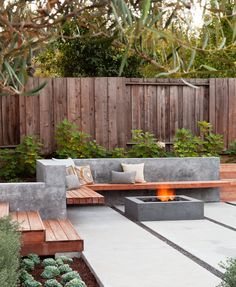 a fire pit in the middle of a patio surrounded by wooden benches and planters