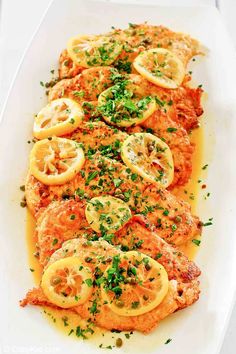 fish with lemons and parsley on top in a white platter, ready to be served