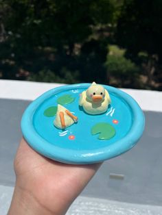 a hand holding a blue frisbee with a rubber duck in the water on it