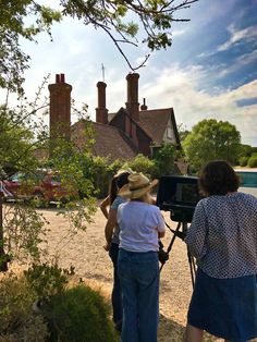 two women standing in front of a house with a camera set up to take pictures